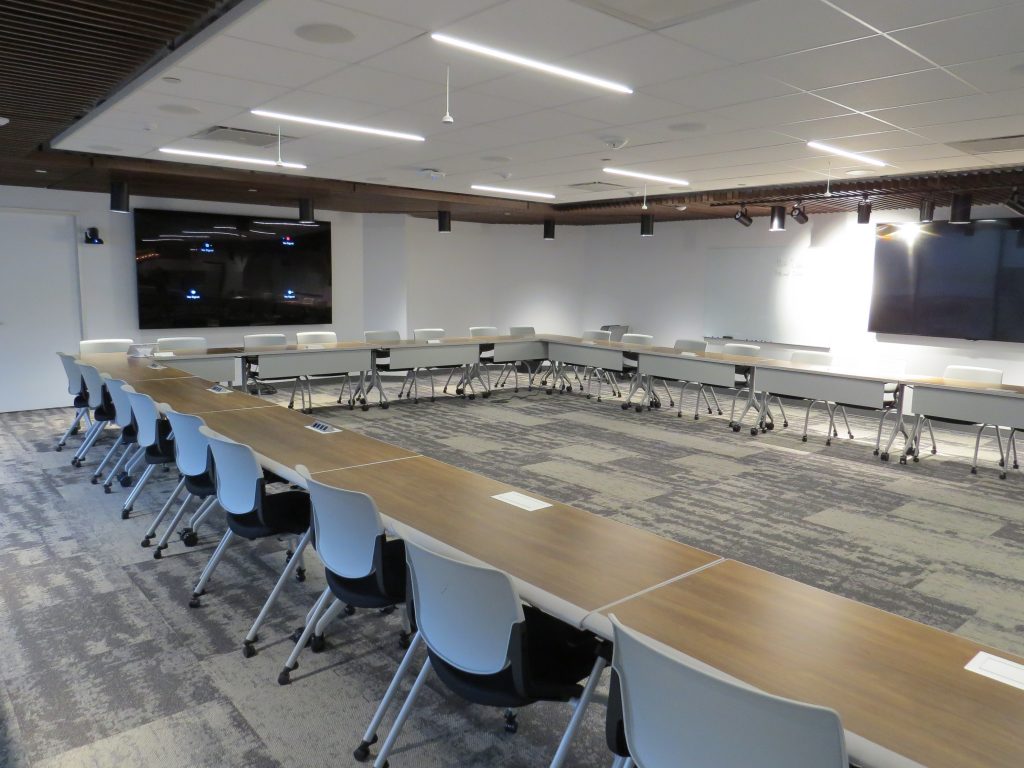 An empty conference room with tables, chairs and large screens